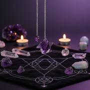 Purple amethyst crystal star pendulum on a silver chain, displayed on a black velvet cloth with white occult symbols, surrounded by glowing candles, crystals, and an amethyst cluster.