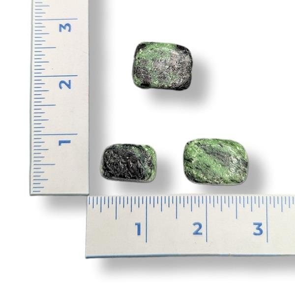 Three green minerals next to a ruler on a white background