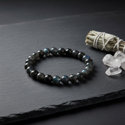 Black beaded bracelet on a dark surface with crystals and sage.