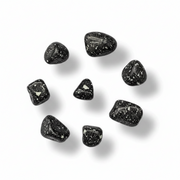 Seven small polished black tumbled stones with white speckles, arranged in a loose circle on a white background with soft drop shadows.