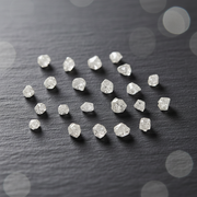 A group of small, rough-cut clear gemstones arranged on a dark textured surface with soft blurred light circles in the background.