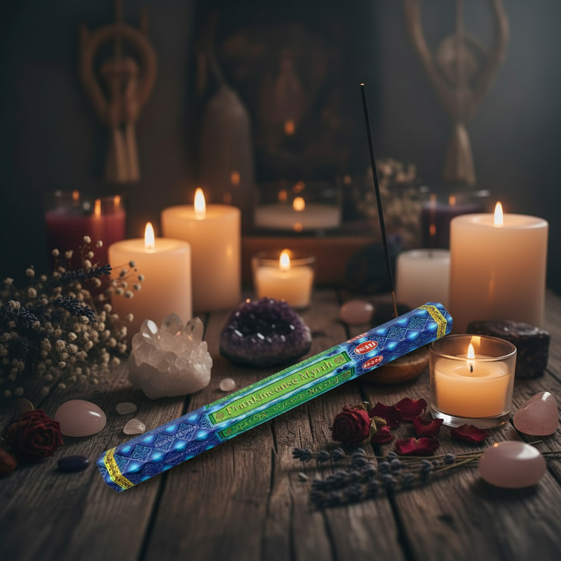 Packaged incense stick with blue and green design on a table surrounded by candles, crystals and flowers.