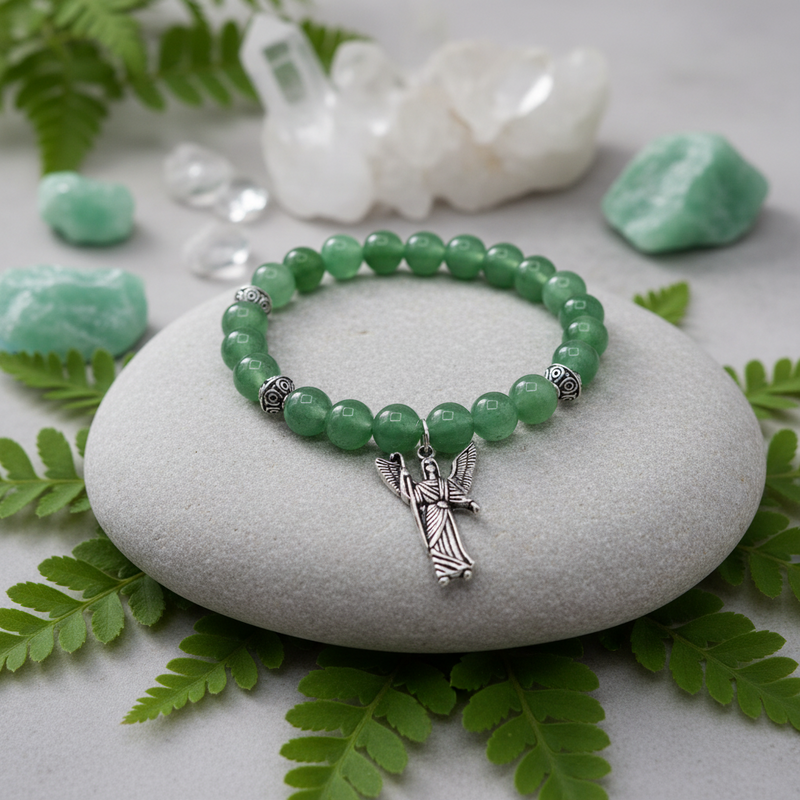 Green beaded bracelet with an angel charm on a white stone surrounded by green leaves and crystals.