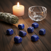 Lapis lazuli tumbled on a wooden table with sage, candle and glass bowl