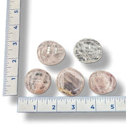 Five round rose quartz stones  with a ruler for scale on a white background