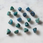 A set of polished tumbled blue-green chrysocolla stones arranged on a white marble surface.
