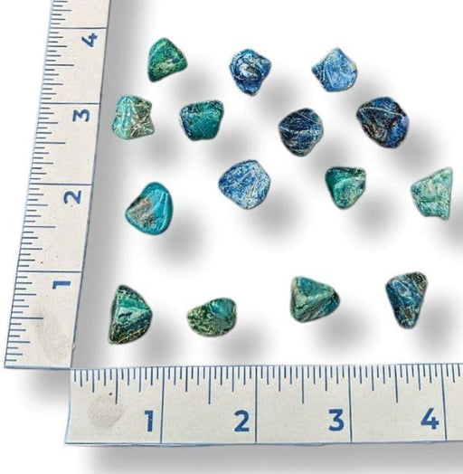 Tumbled chrysocolla stones with a ruler for scale on a white background