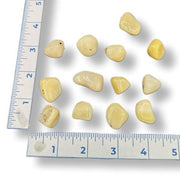 A series of tumbled yellow opal stones of varying sizes, displayed in front of a blue measuring tape for scale.