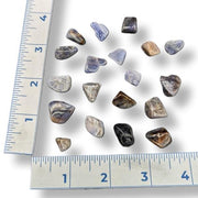 A collection of tumbled tanzanite stones of various shades of blue and purple, placed on a surface with a ruler for scale.