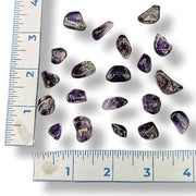 Tumbled purple brandberg quartz gemstones scattered on a white background with a ruler on the left and bottom edges for size reference.