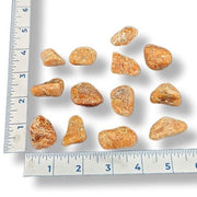 Orange calcite stones of various sizes on a white background with a ruler for scale.