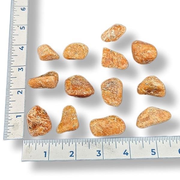 Orange calcite stones of various sizes on a white background with a ruler for scale.