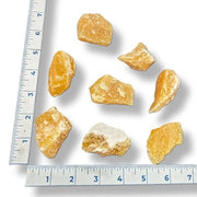 Raw orange calcite stones with a ruler for scale on a white background