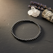 Black beaded bracelet on a dark surface with crystals and lavender.