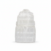 A white selenite tower figurine made of stacked, tiered selenite crystals, photographed on a seamless white background.