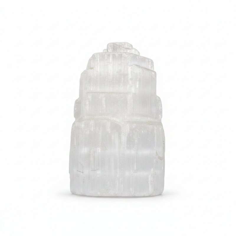 A white selenite tower figurine made of stacked, tiered selenite crystals, photographed on a seamless white background.