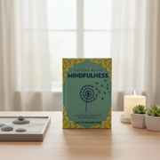 Book titled 'A Little Bit of Mindfulness' on a table with a candle and plants in the background.