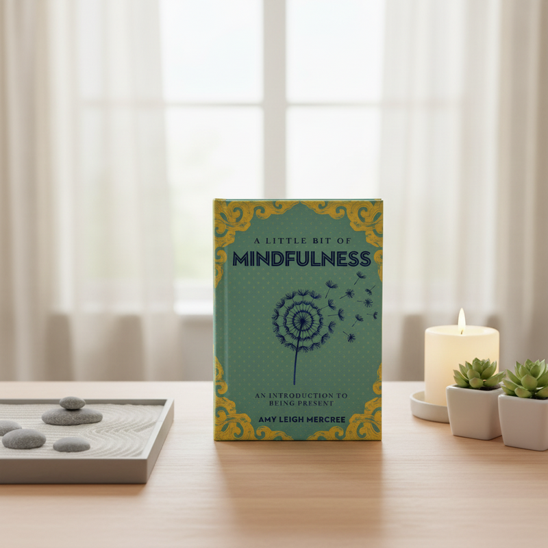 Book titled 'A Little Bit of Mindfulness' on a table with a candle and plants in the background.