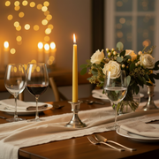 Dining table set for a romantic dinner with wine glasses, candles, and flowers.
