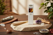 A box of Nitraj Nirvana incense sticks stands upright on a stone slab, surrounded by incense sticks, a smudge bundle, crystals, lavender, and dried flowers on a wooden table.