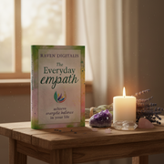 Book titled 'The Everyday Empath' by Raven Digitalis on a wooden table with a candle and crystals.