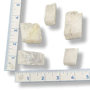 Five pieces of white stone or crystal on a white background with a ruler for scale.