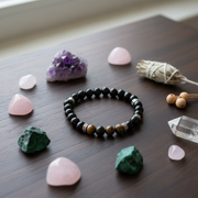 Black beaded bracelet on a wooden surface with crystals and a smudge stick.