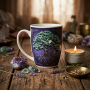 A ceramic mug with a white handle and rim, decorated with a dark purple background and a detailed illustration of a green tree with white roots, set on a rustic wooden table with crystals, a lit candle, and dried herbs.