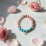 Bracelet with pink and blue beads on a marble surface with flowers and macarons.