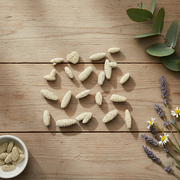 Natural beige calcite sand arranged on a rustic wooden tabletop, with a small white bowl of more chews in the lower left and green leaves and daisies in the upper right.