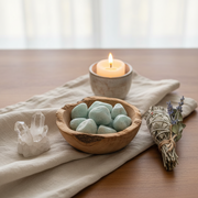 Bowl of stones, candle, crystal, and sage on a cloth-covered surface