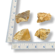 Four pieces of honey calcite on a ruler for scale measurement.