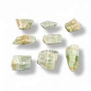 Nine raw, rough calcite with natural striated patterns in pale green, beige, and cream, arranged in a 3x3 grid on a white background with soft drop shadows.