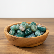 Wooden bowl filled with green stones on a wooden surface