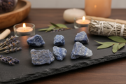 Six raw blue aventurine crystal stones arranged on a dark slate tray, styled with lavender sprigs, a sage bundle, and lit candles in a warm, cozy setting.