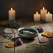 A mystical setting with candles, crystals, and a sage bowl on a wooden surface.