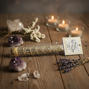 Sage in a clear packaging on a wooden surface with candles, crystals, and lavender.