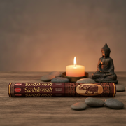 Sandalwood incense sticks with a lit candle and Buddha statue on a wooden surface.