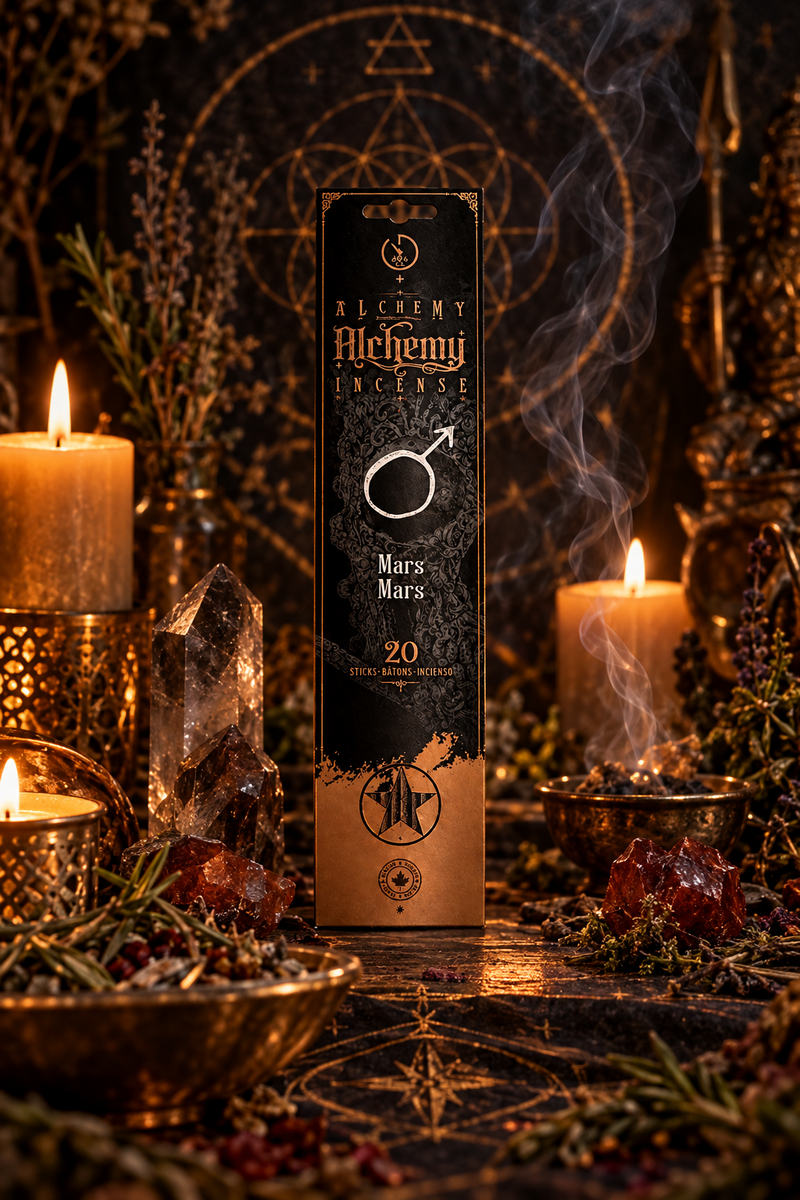 A tall rectangular box of Alchemy Incense labeled Mars, standing in a dark, mystical arrangement with lit candles, crystals, herbs, and visible smoke. The box is black with gold lettering and a gold ring-and-arrow symbol.
