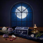 Moon Magick product with crystals, lavender, and a candle on a table with a window showing a full moon.