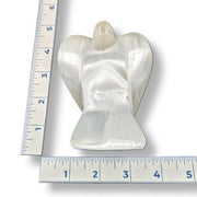 White selenite angel figurine next to a ruler on a white background