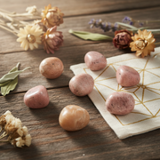 Pink stones on a wooden surface with dried flowers and a geometric-patterned cloth.