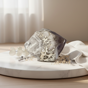 an amethyst point displayed on a round white marble board with white fabric and dried flowers in a softly lit interior setting.