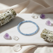 Blue beaded bracelet on a white surface with crystals and sage.