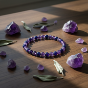 Purple and blue beaded bracelet on a wooden surface with amethyst crystals and leaves.