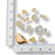 Ten small translucent amber and pale grayish-brown pieces arranged on a white background with ruler edges visible along the left and bottom for scale.