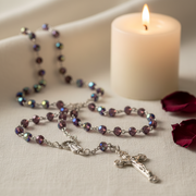 Glass Birthstone Rosary for February next to a lit candle on a soft surface.