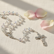 Rosary that symbolizes the Birthstone April on a light fabric background with pink petals.