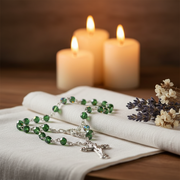 Glass Birthstone Rosary for May on a white cloth with lit candles in the background