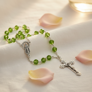 Glass Birthstone Rosary  for August on a white surface with pink petals.